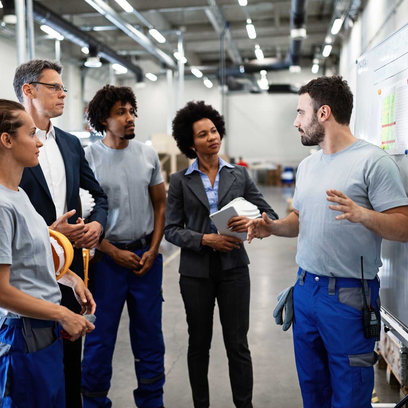A group of workers in a warehouse having a standing meeting.